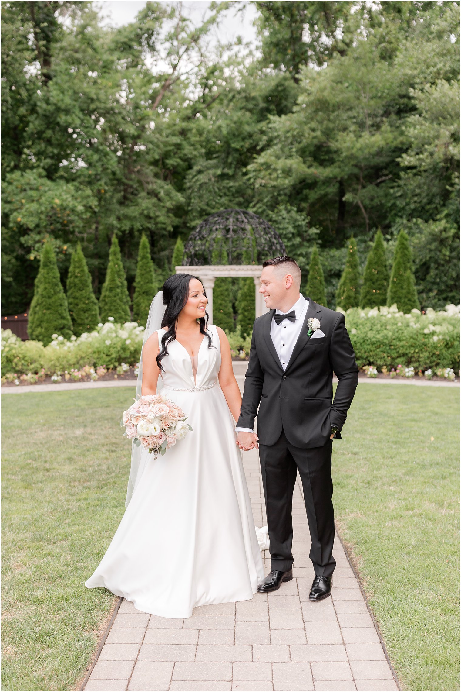 newlyweds hold hands walking on path in Hamilton Manor garden