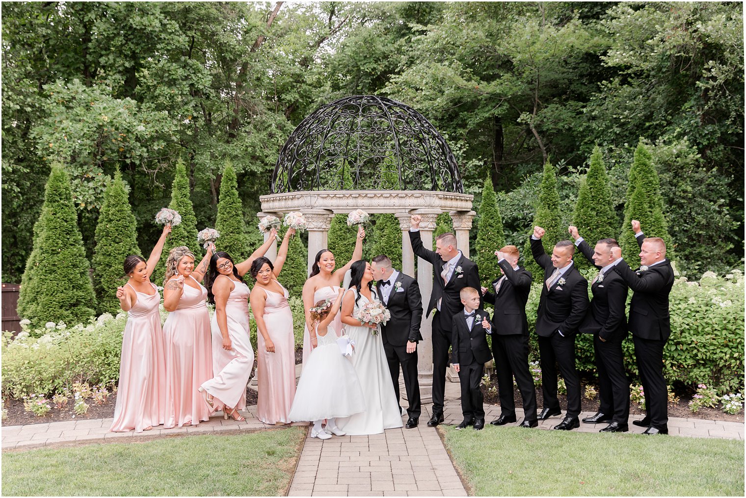 bride and groom kiss while wedding party cheers by gazebo at Hamilton Manor