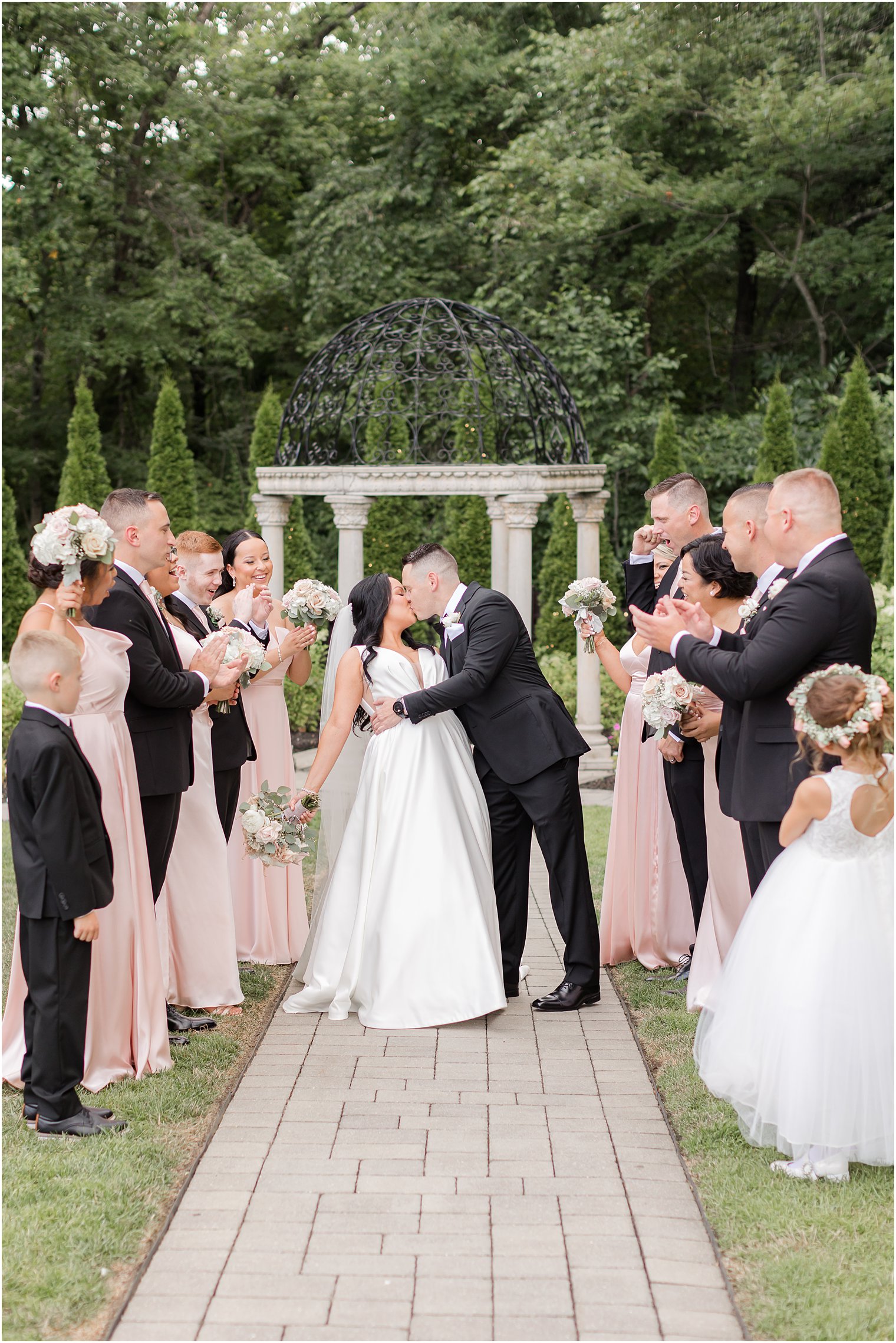 newlyweds kiss with wedding party around them at Hamilton Manor