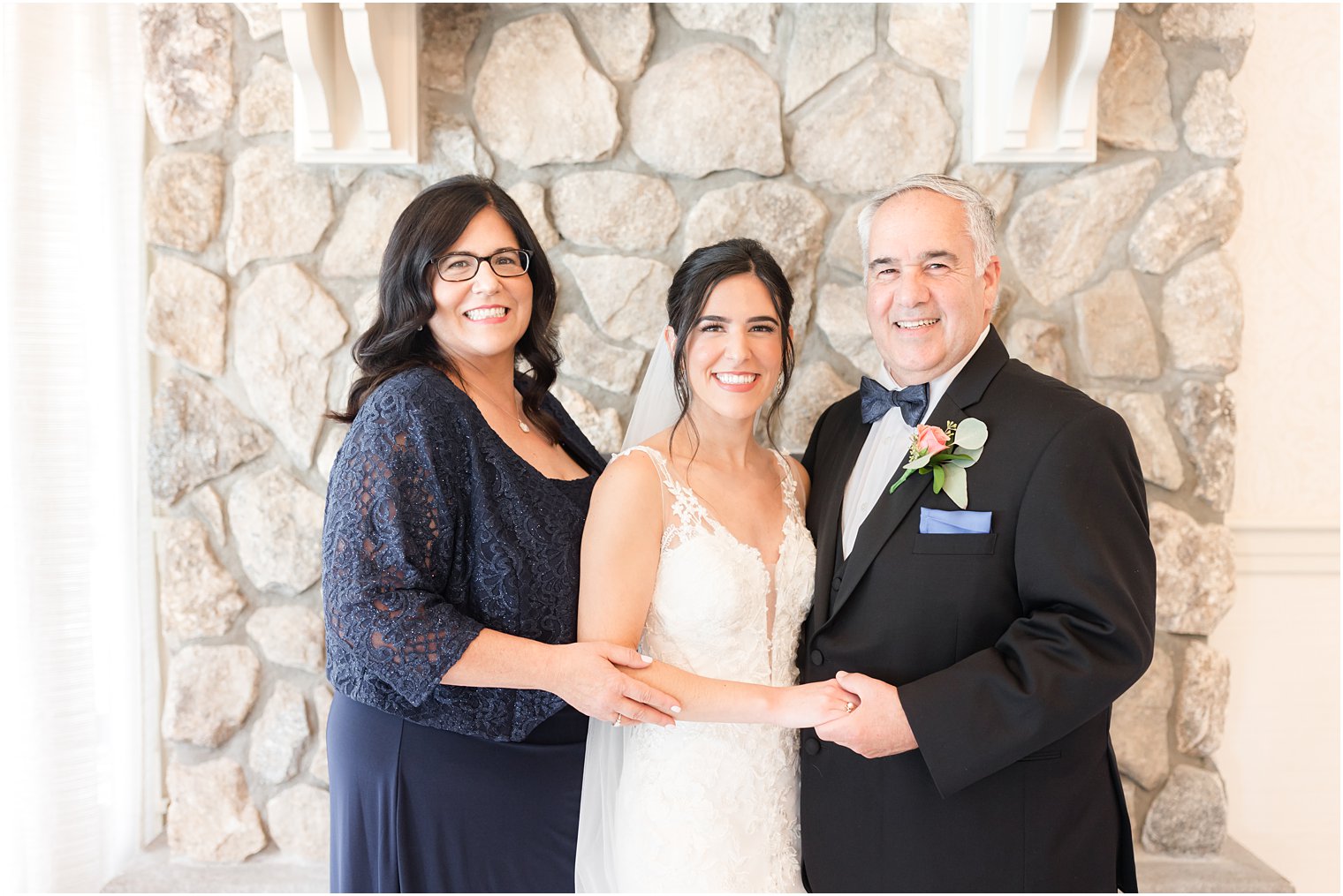 bride stands with parents by stone fireplace