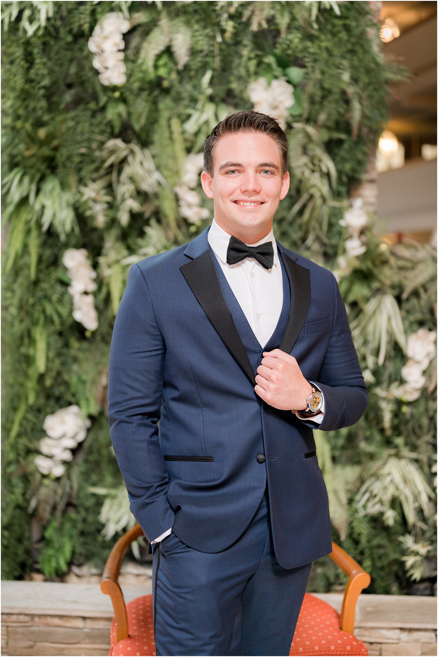 groom stands in navy suit with black lapels