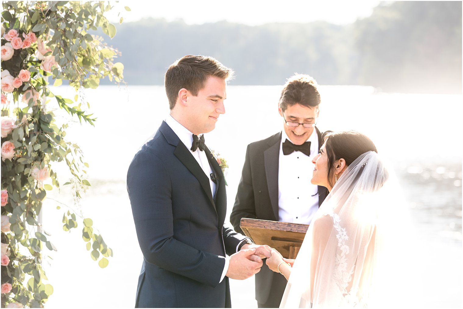groom smiles at bride during outdoor wedding ceremony by water in Franklin Lakes NJ