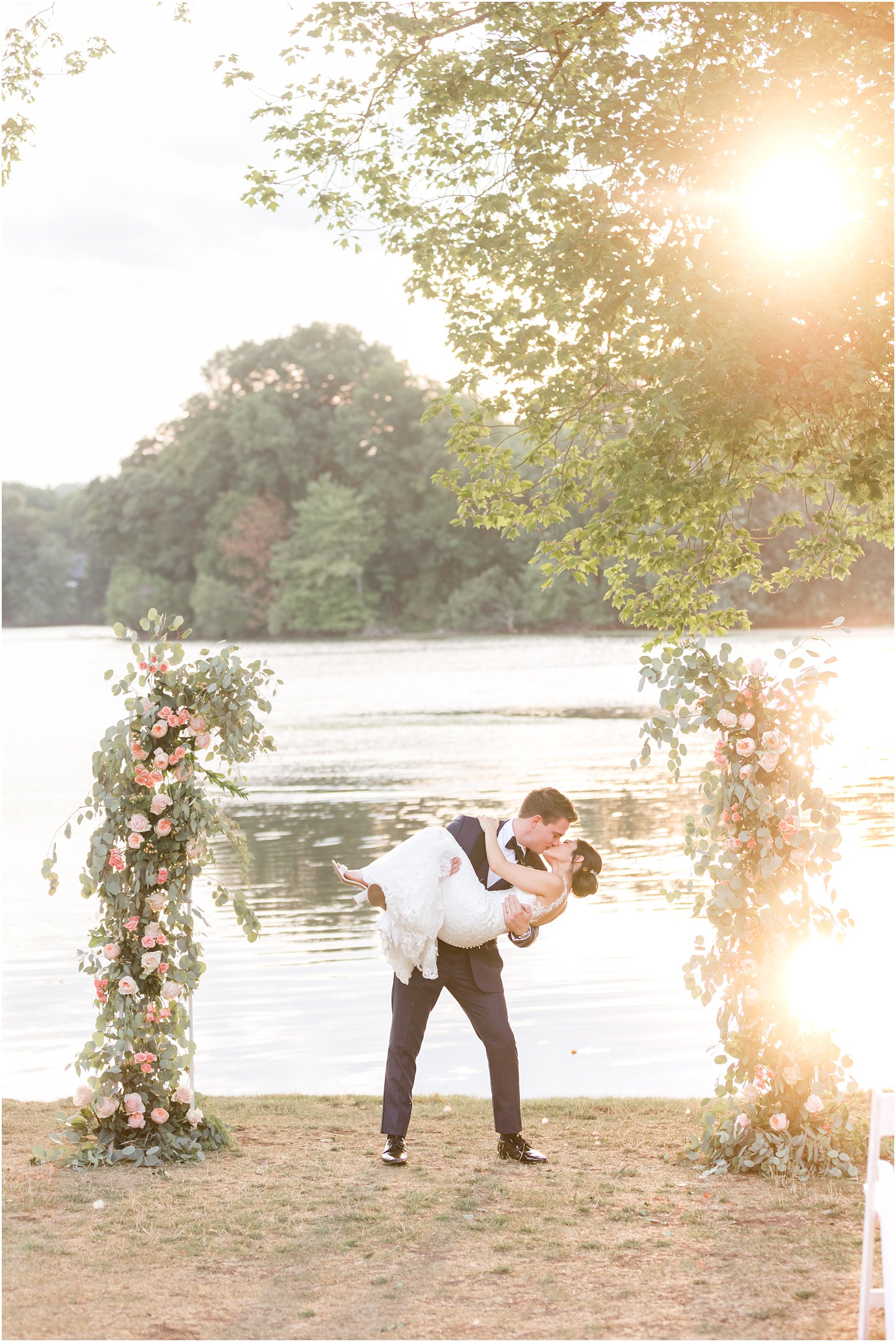 groom lifts up bride at sunset between floral arches along waterfront 