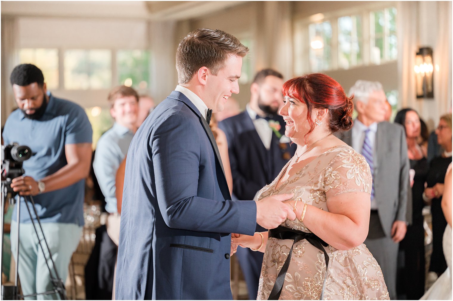 groom in navy suit dances with mother in gold gown