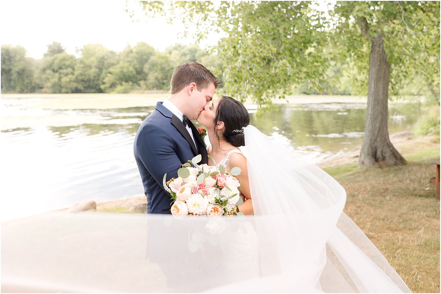 bride and groom kiss with veil around them along waterfront at Indian Trail Club