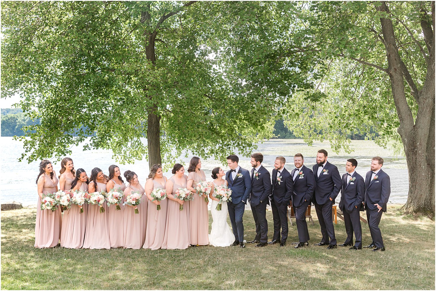 bride and groom smile at each other while bridal party looks at them