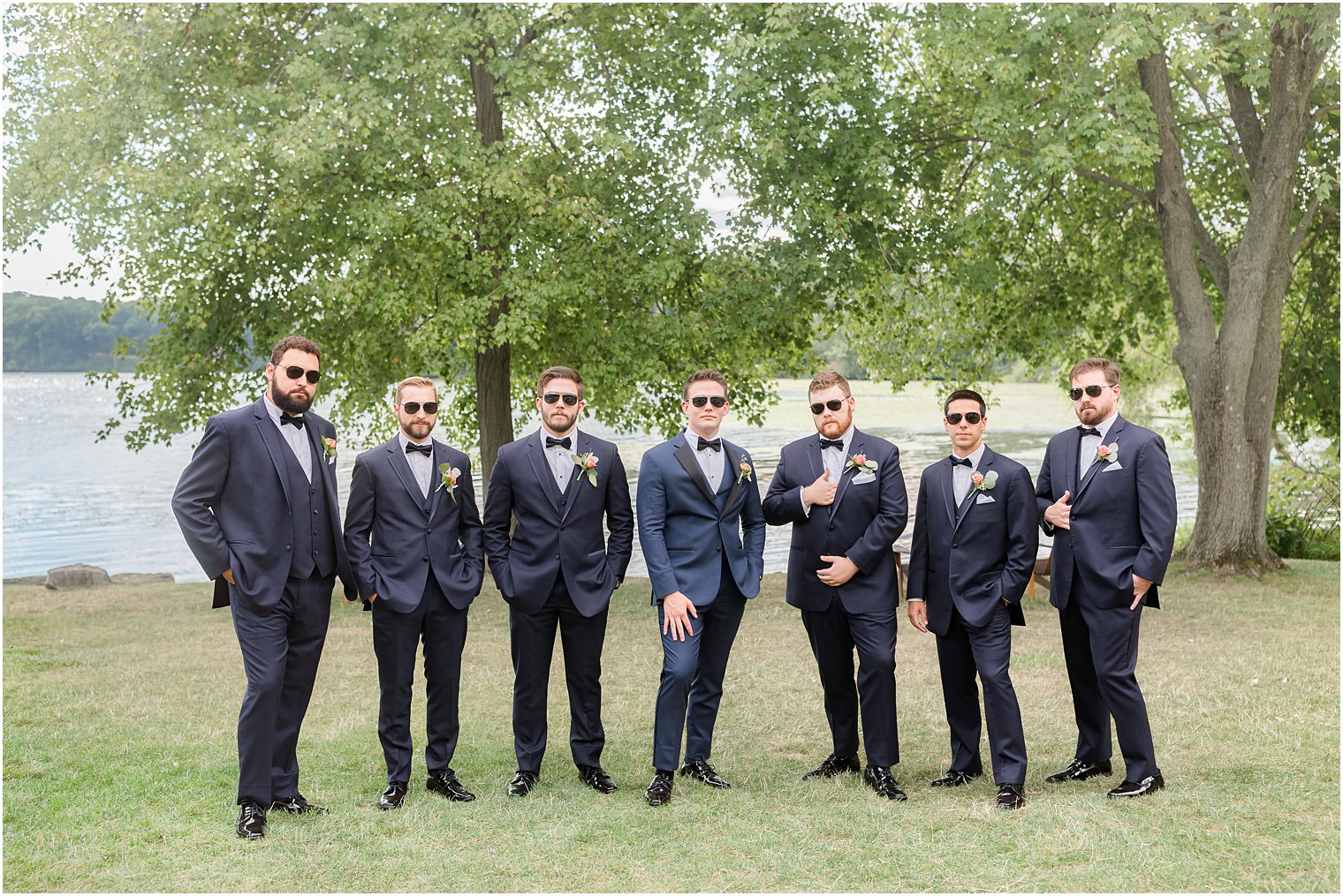groom stands with groomsmen in navy suits with sunglasses