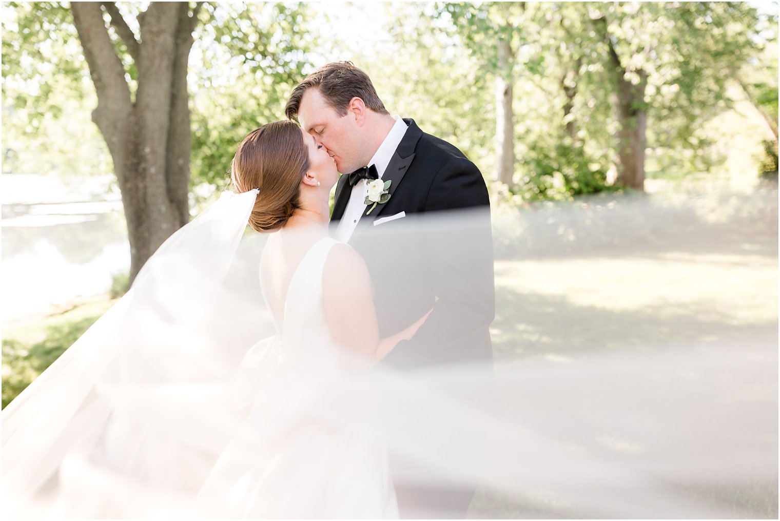 bride and groom kiss while veil floats around them