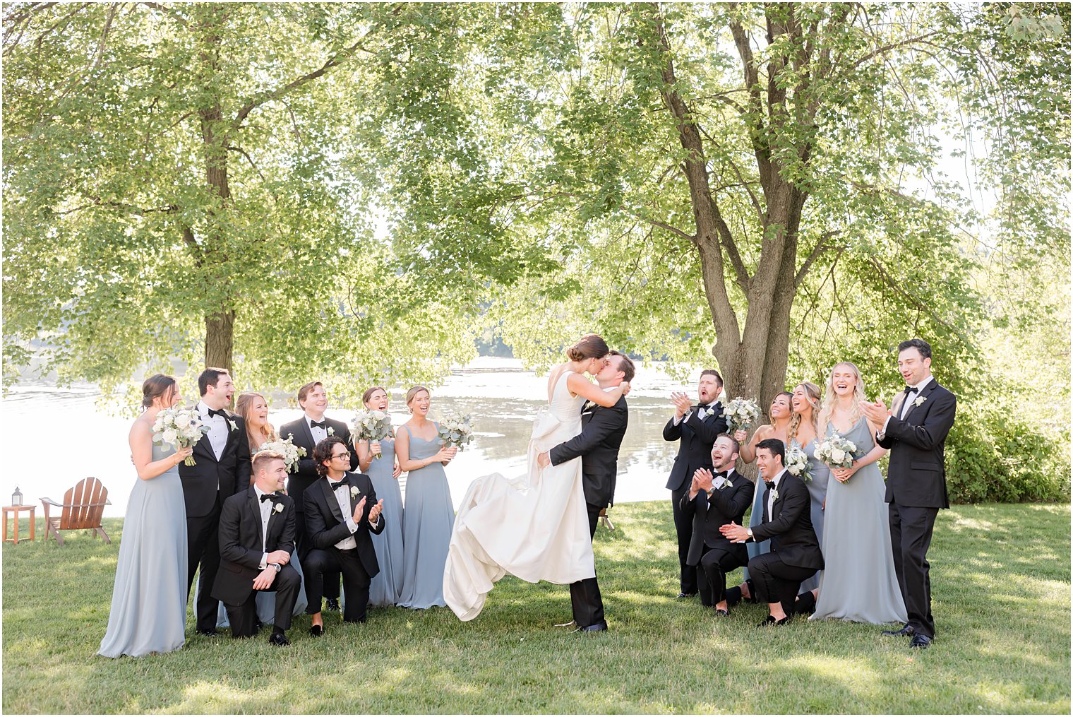 groom lifts bride kissing her while bridal party cheers