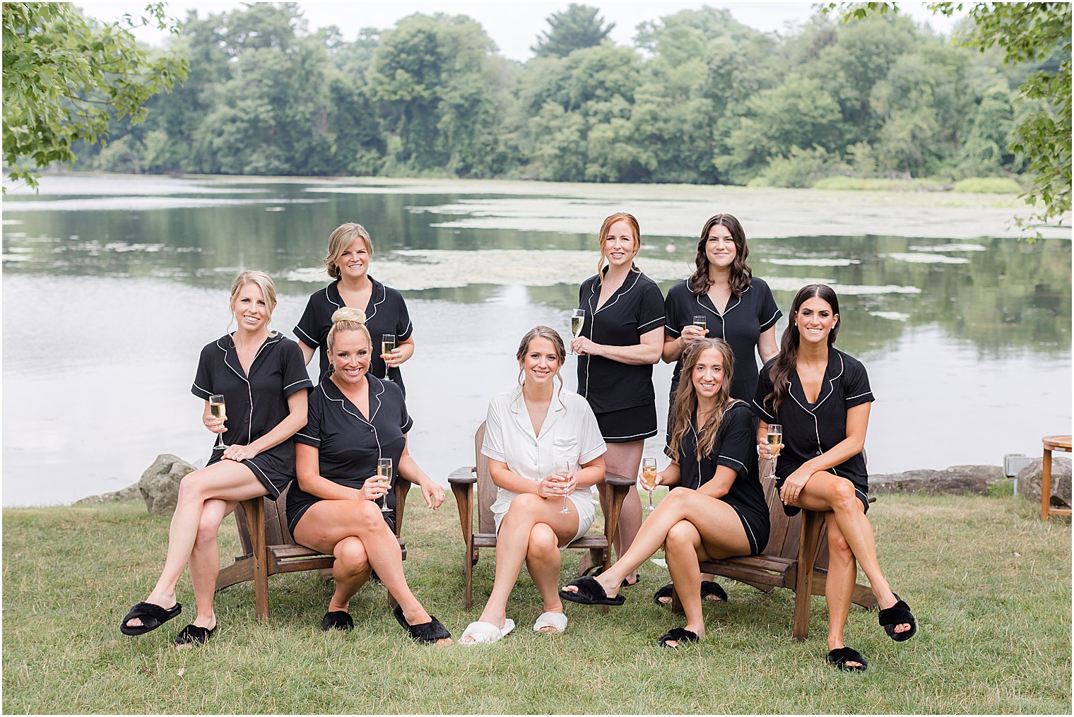 bride sits with bridesmaids in black pajamas by lake at Indian Trail Club