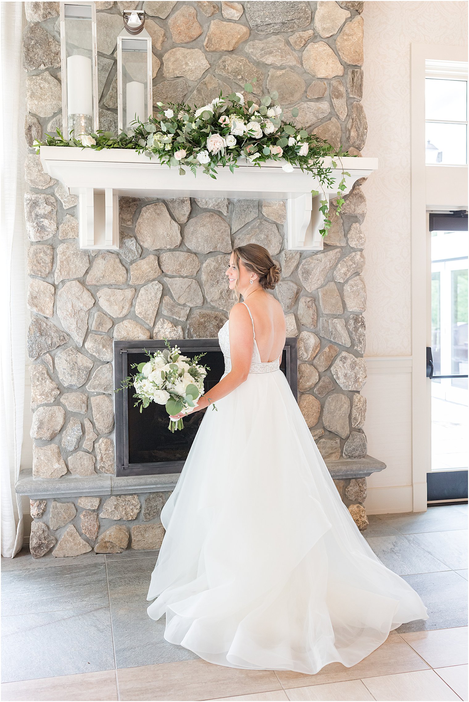bride poses by stone fireplace holding bouquet of white flowers at Indian Trail Club