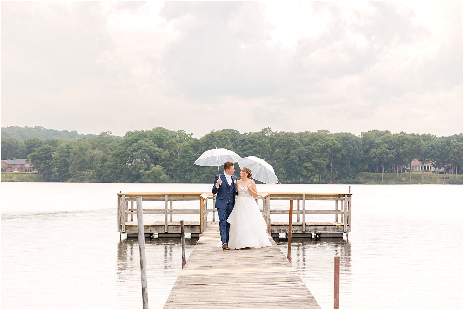 couple walks on dock at Indian Trail Club under clear umbrella
