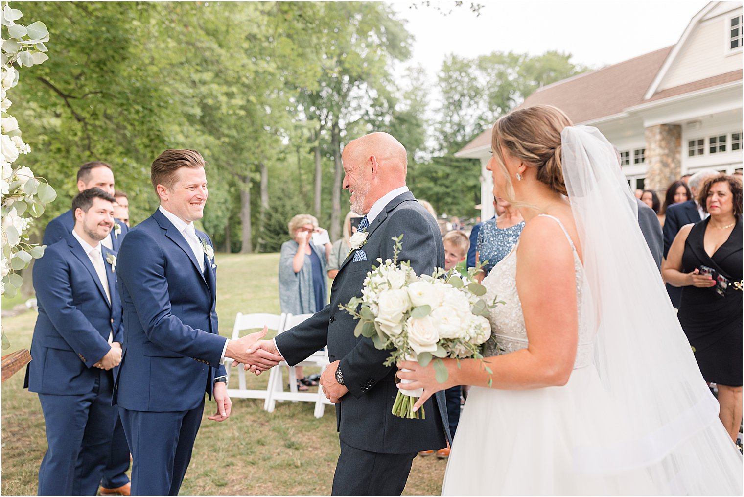 dad shakes groom's hand during outdoor wedding ceremony by water at Indian Trail Club