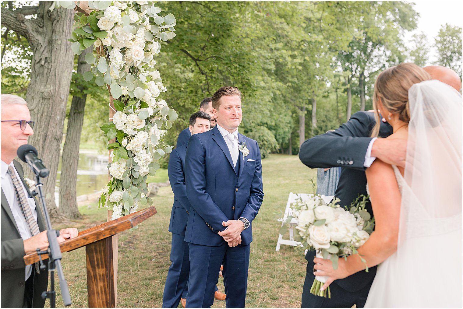 groom smiles at bride before outdoor wedding ceremony by water at Indian Trail Club