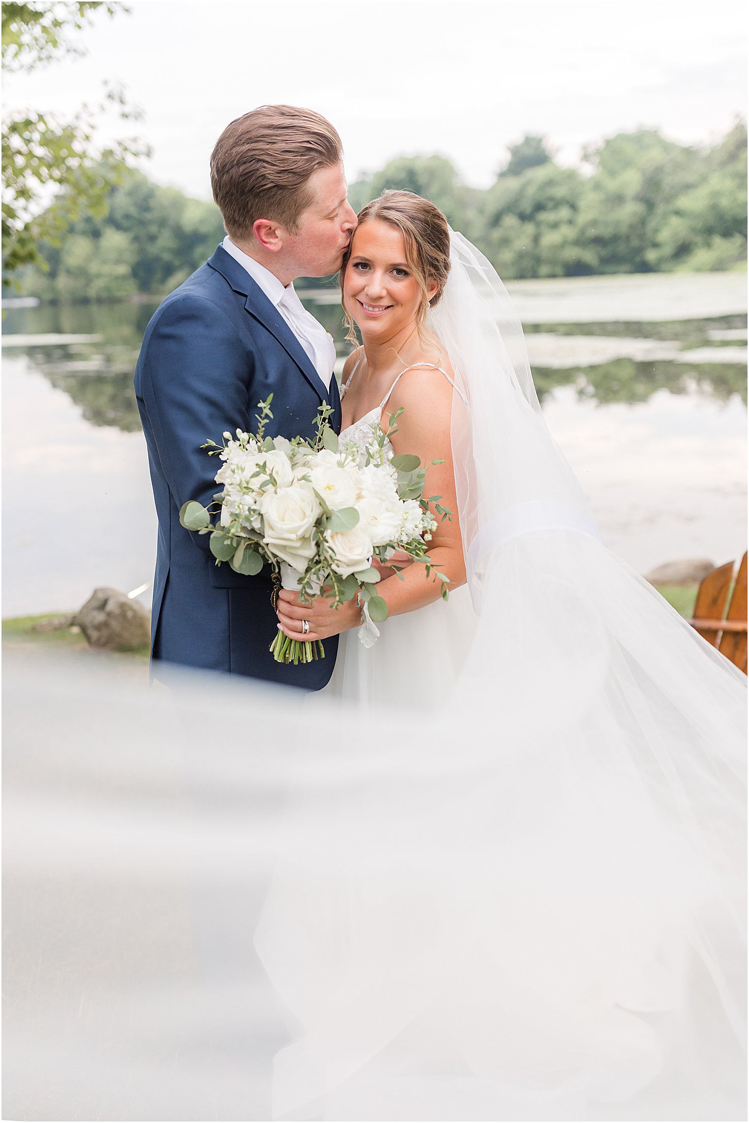 groom kisses bride's forehead with veil draped around them