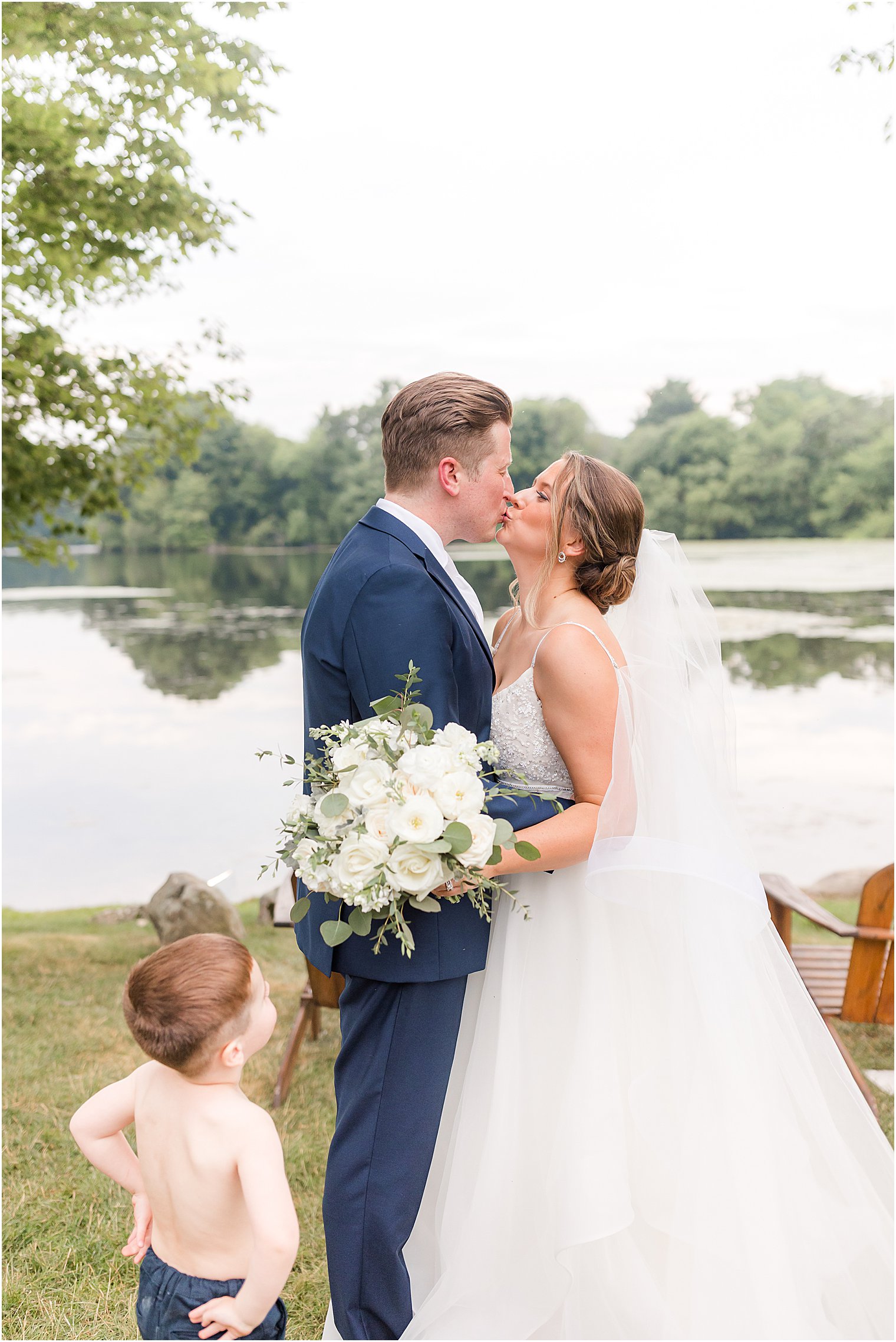 bride and groom kiss while ring bearer watches