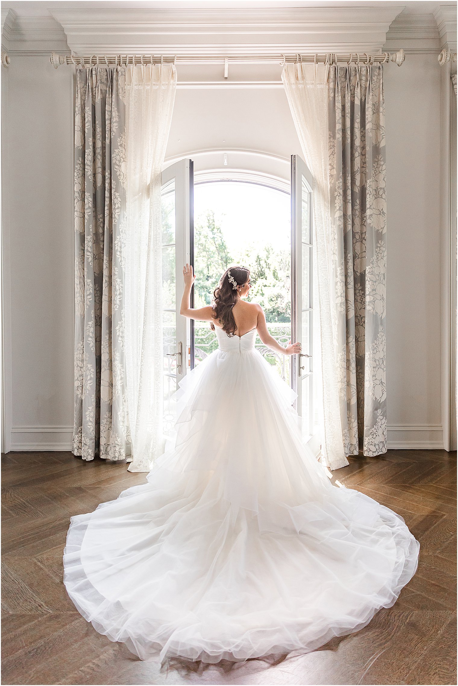 bride looks out window at Park Chateau Estate with gown around her