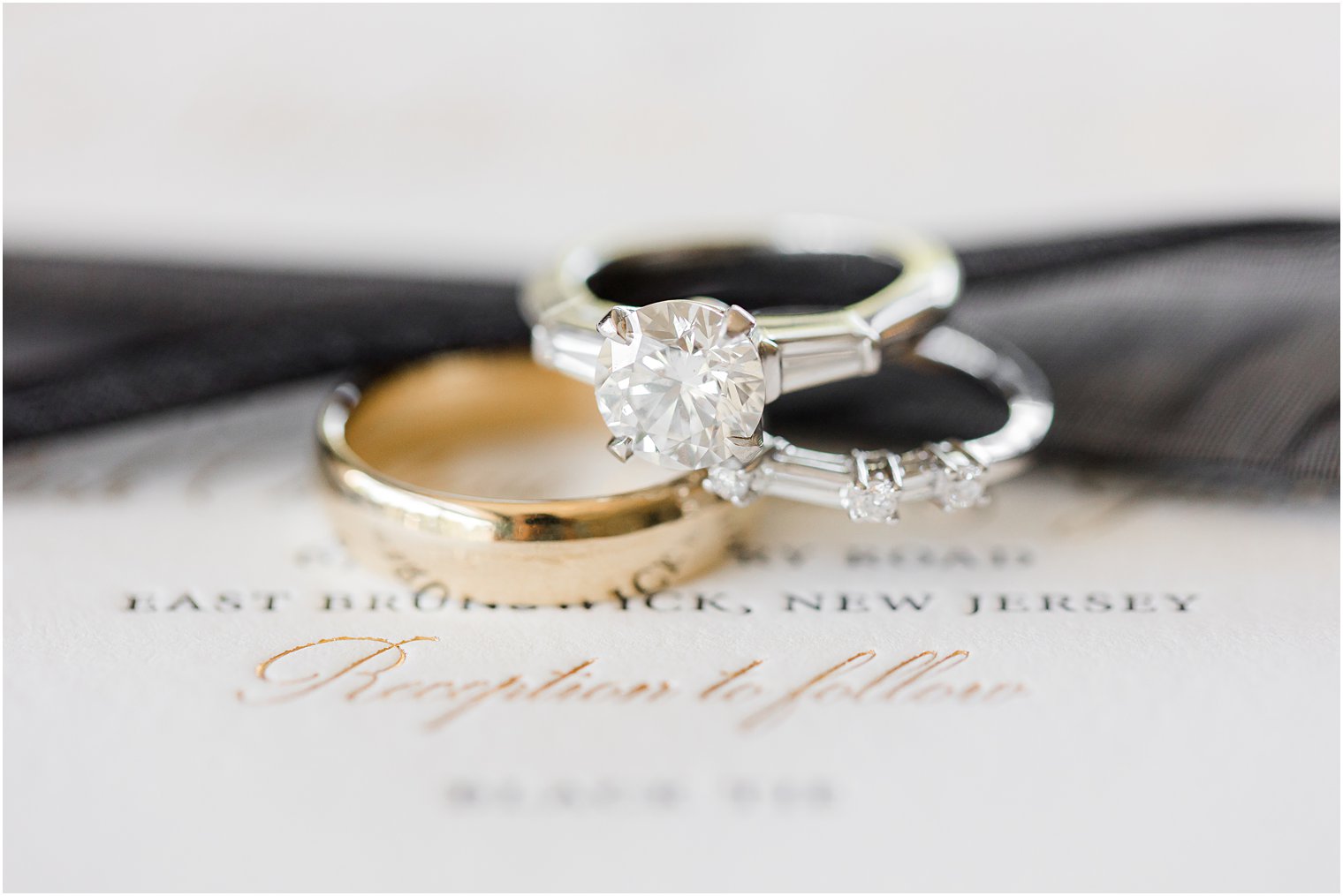 wedding rings rest on black ribbon and invitation suite 