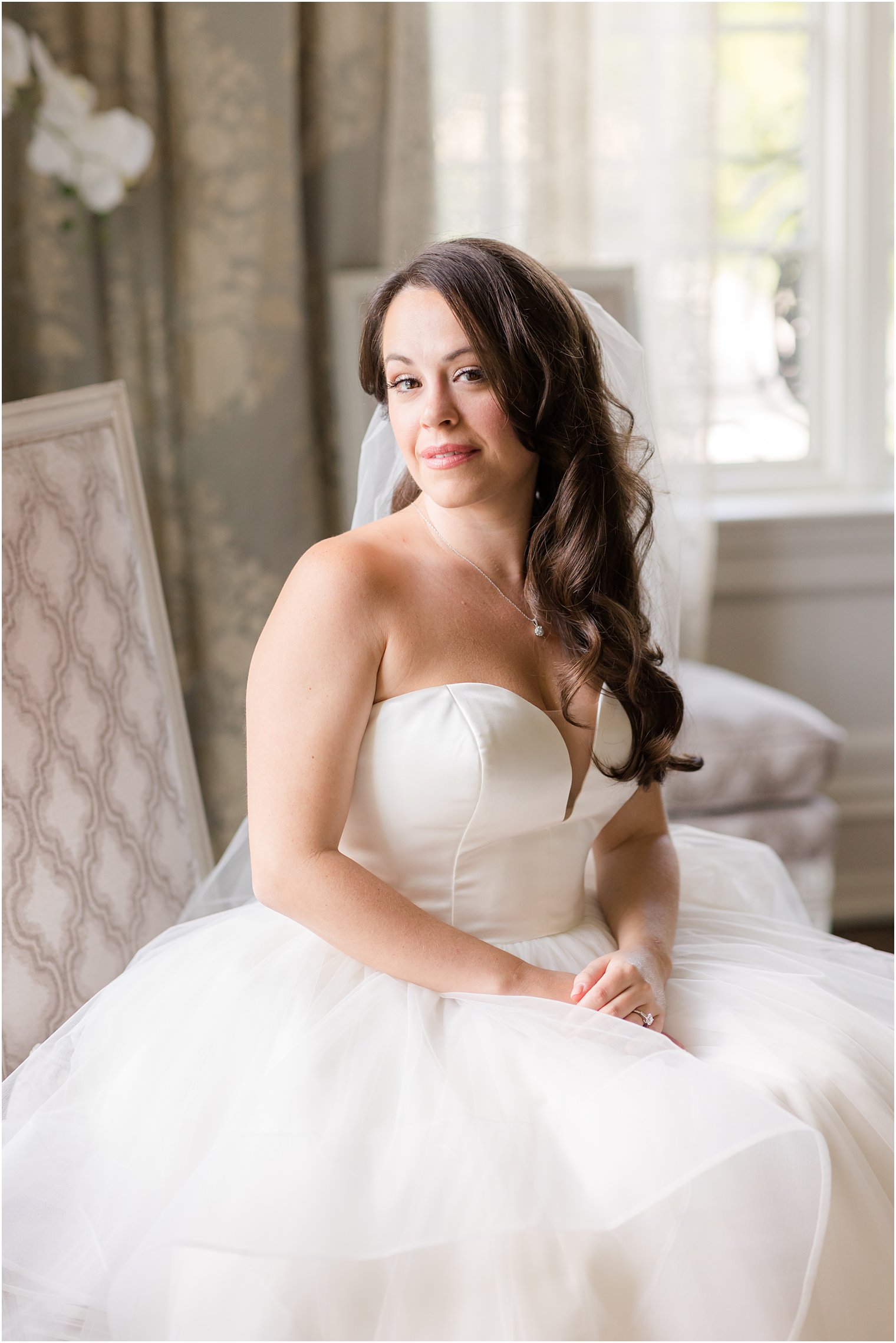 bride sits in grey chair at Park Chateau Estate with veil behind her