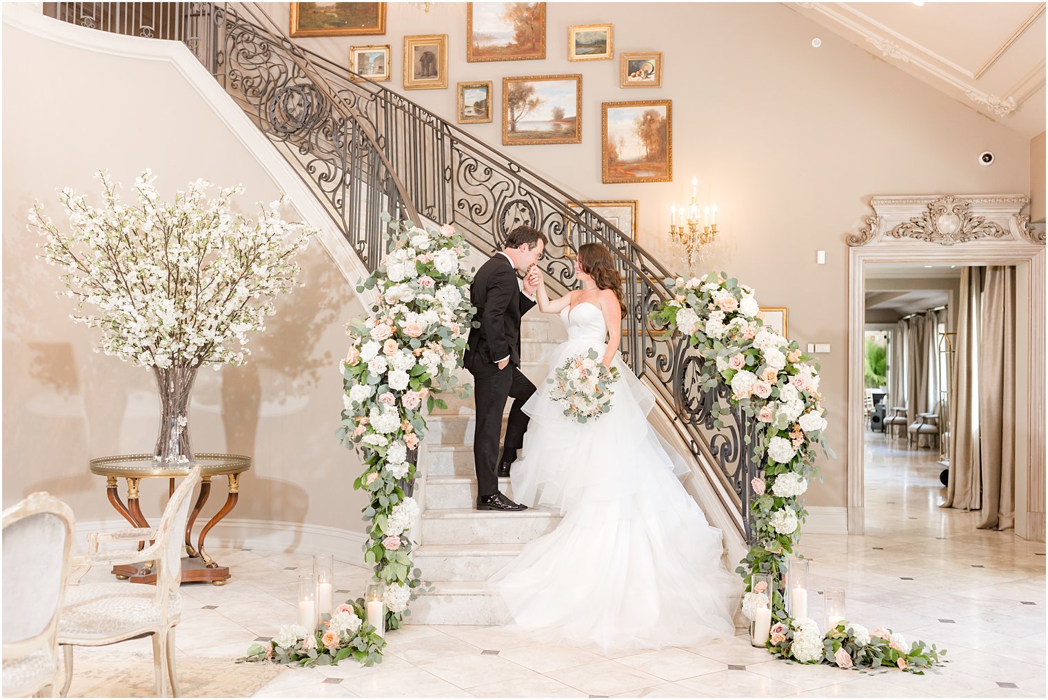 groom kisses bride's hand on staircase with cascading florals