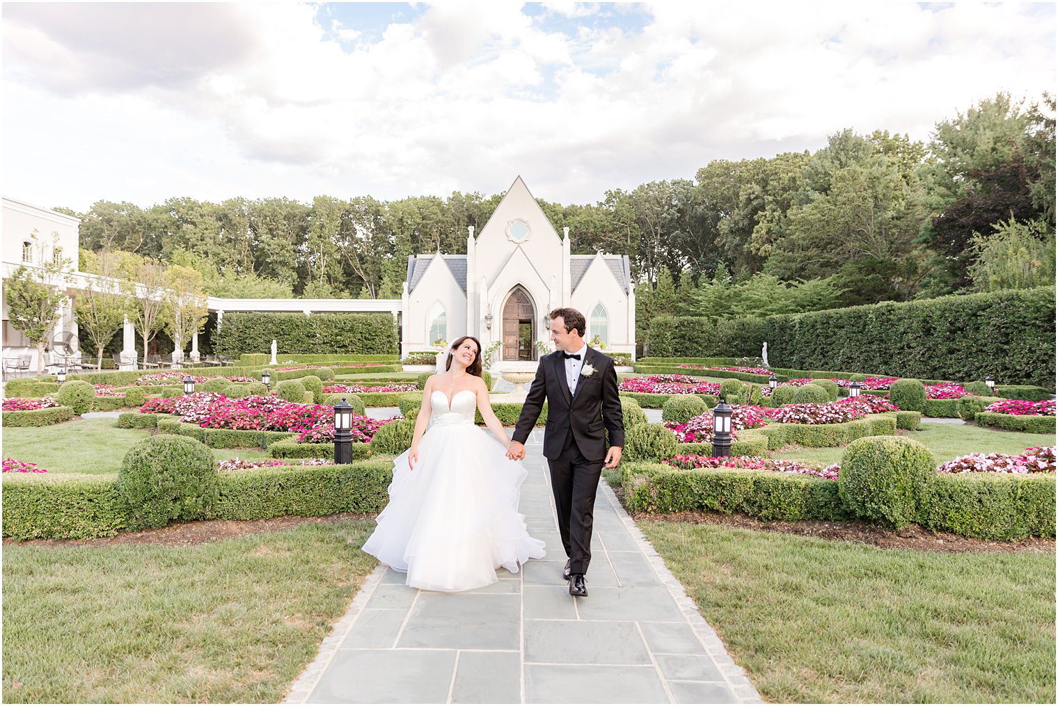 bride and groom hold hands walking through French Garden in Park Chateau Estate