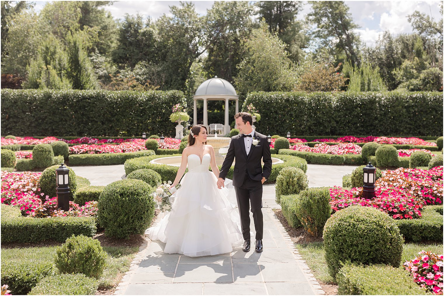 bride and groom hold hands walking through pink and green flowers at Park Chateau Estate