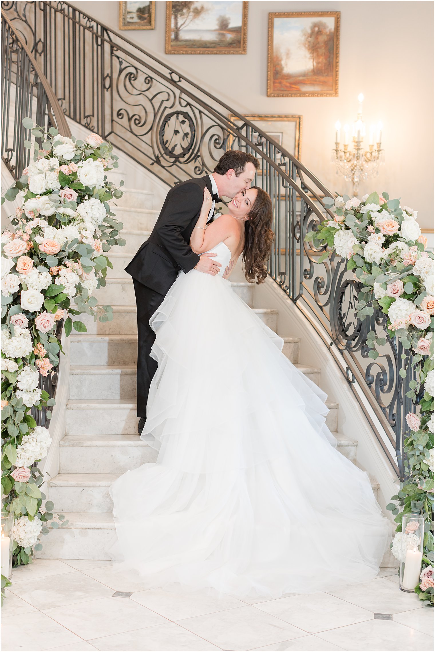 groom kisses bride's cheek on staircase with flowers at Park Chateau Estate