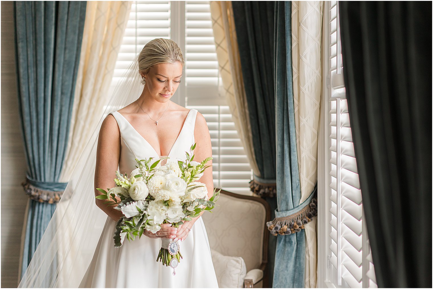 bride stands by window with teal curtains at Shadowbrook at Shrewsbury