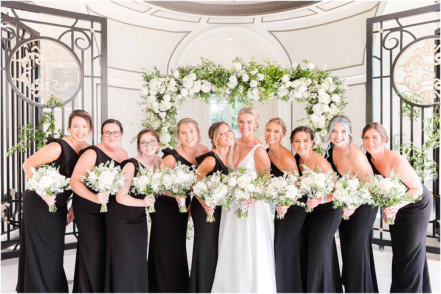 bride stands with bridesmaids in black gowns with white bouquets 