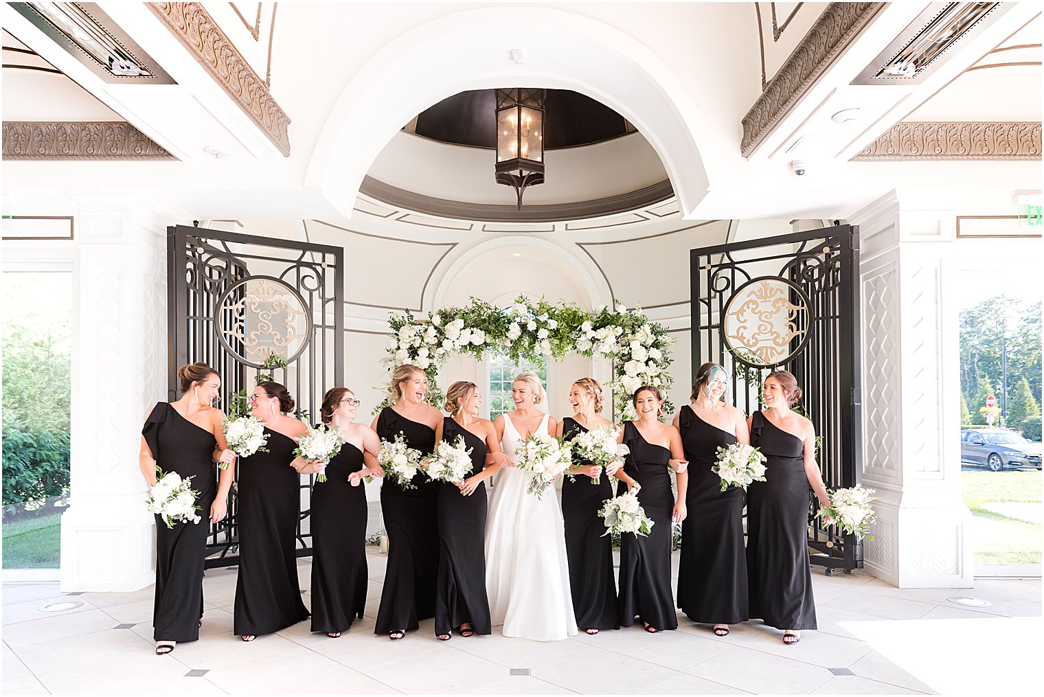bride stands with bridesmaids in black gowns holding white bouquets