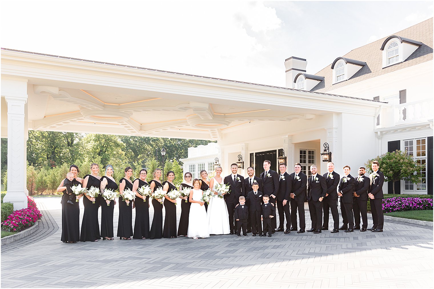 bride and groom pose with wedding party in black gowns with classic tuxes