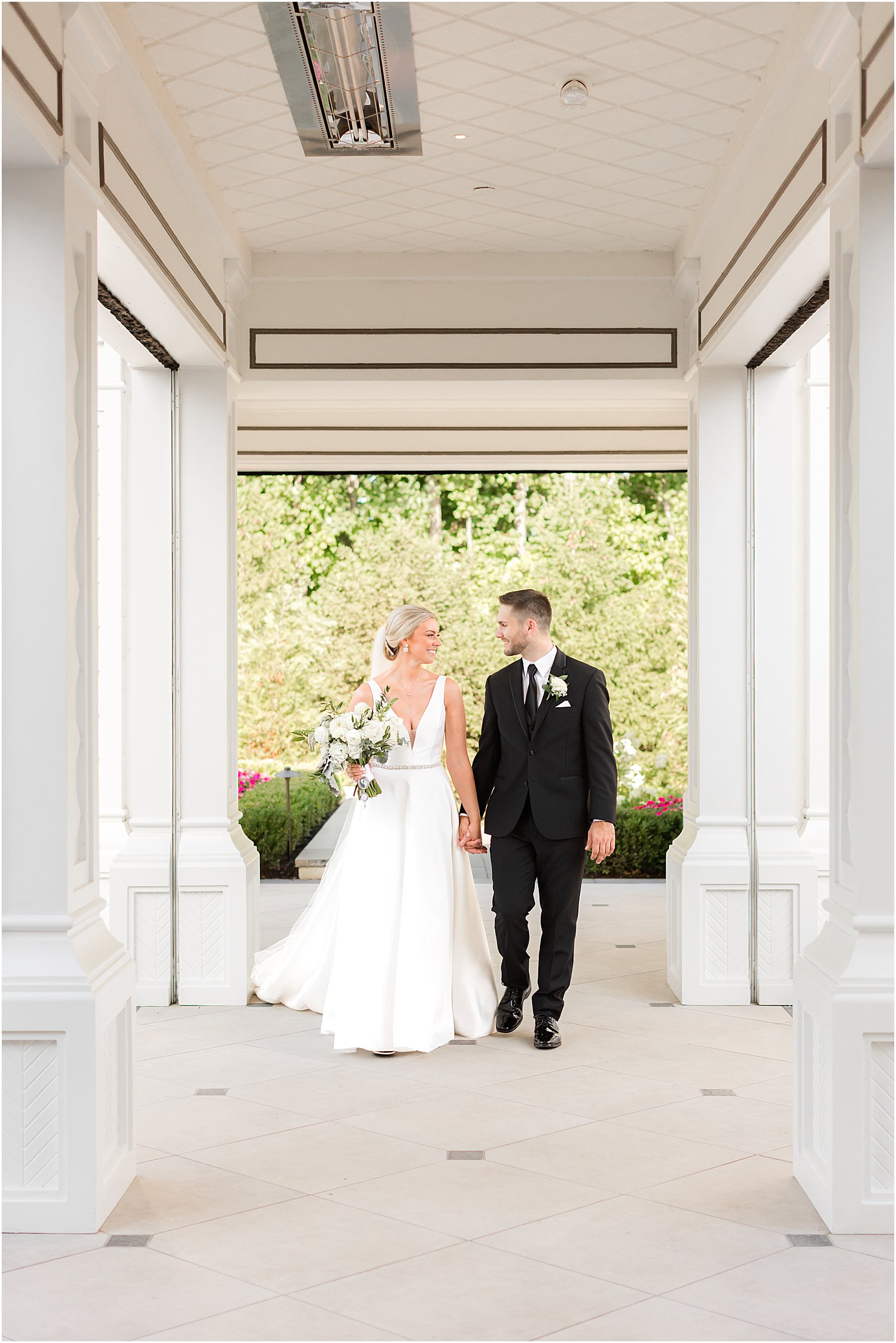 newlyweds hold hands walking through patio at Shadowbrook at Shrewsbury