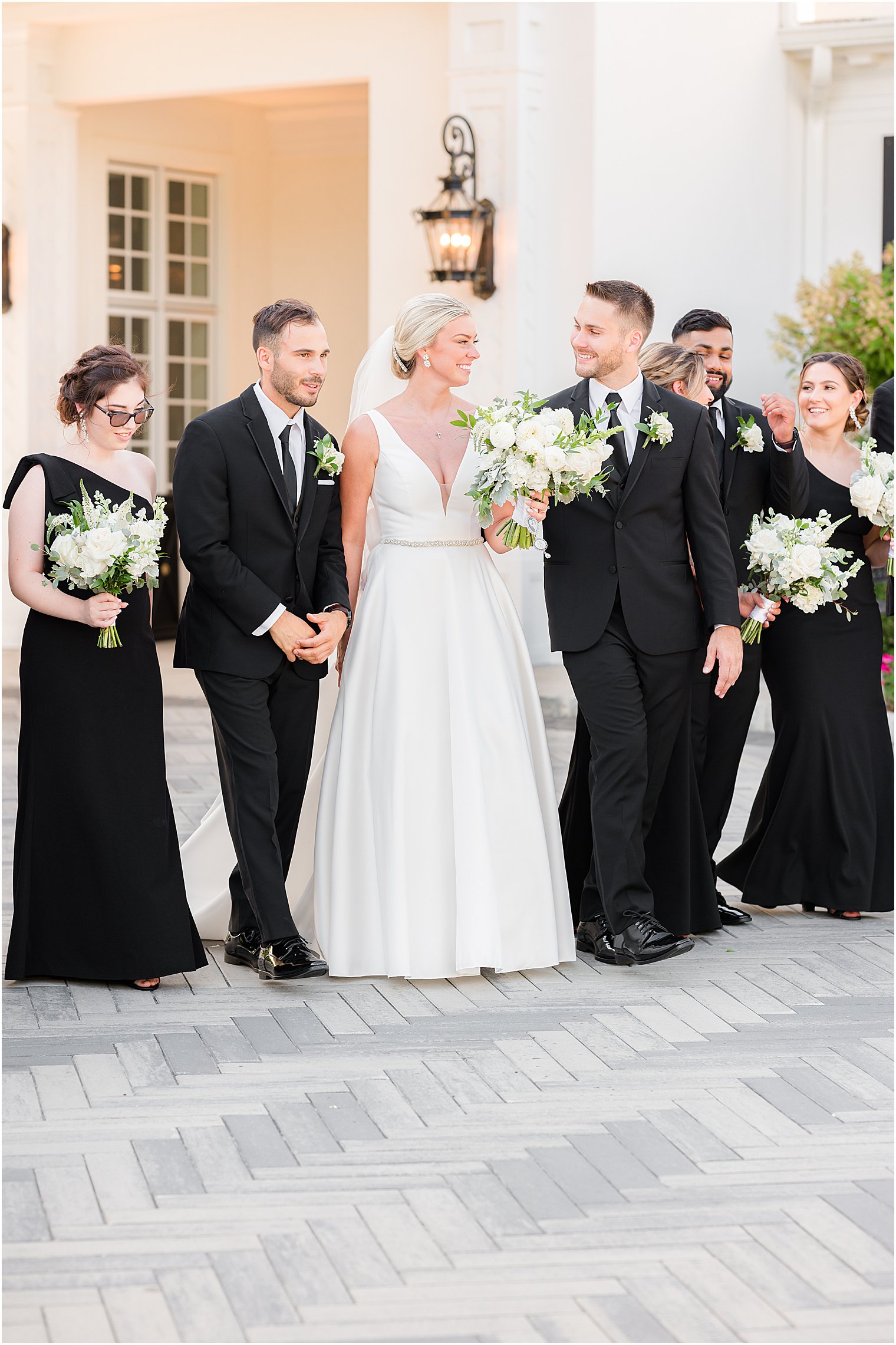 bride and groom smile while wedding party waits around them at Shadowbrook at Shrewsbury