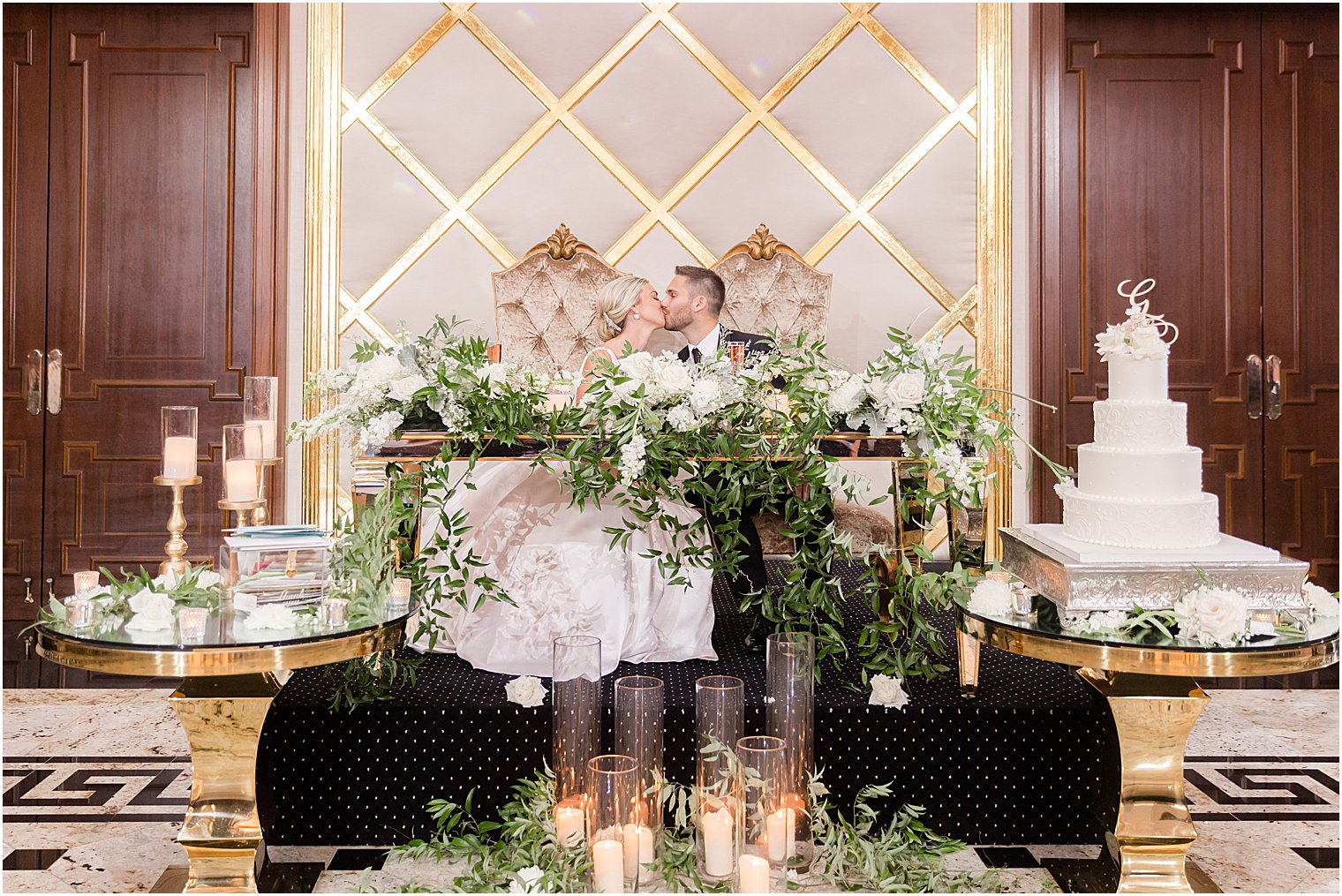 newlyweds sit at sweetheart table with greenery draped around front