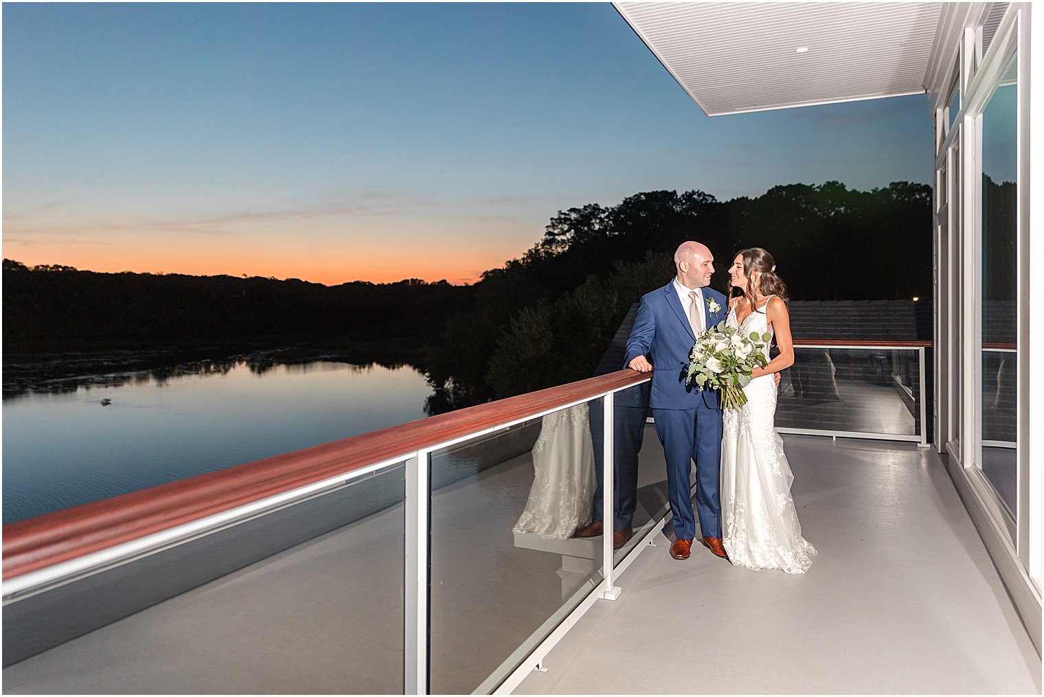 newlyweds stand on balcony at sunset at The Mill Lakeside Manor