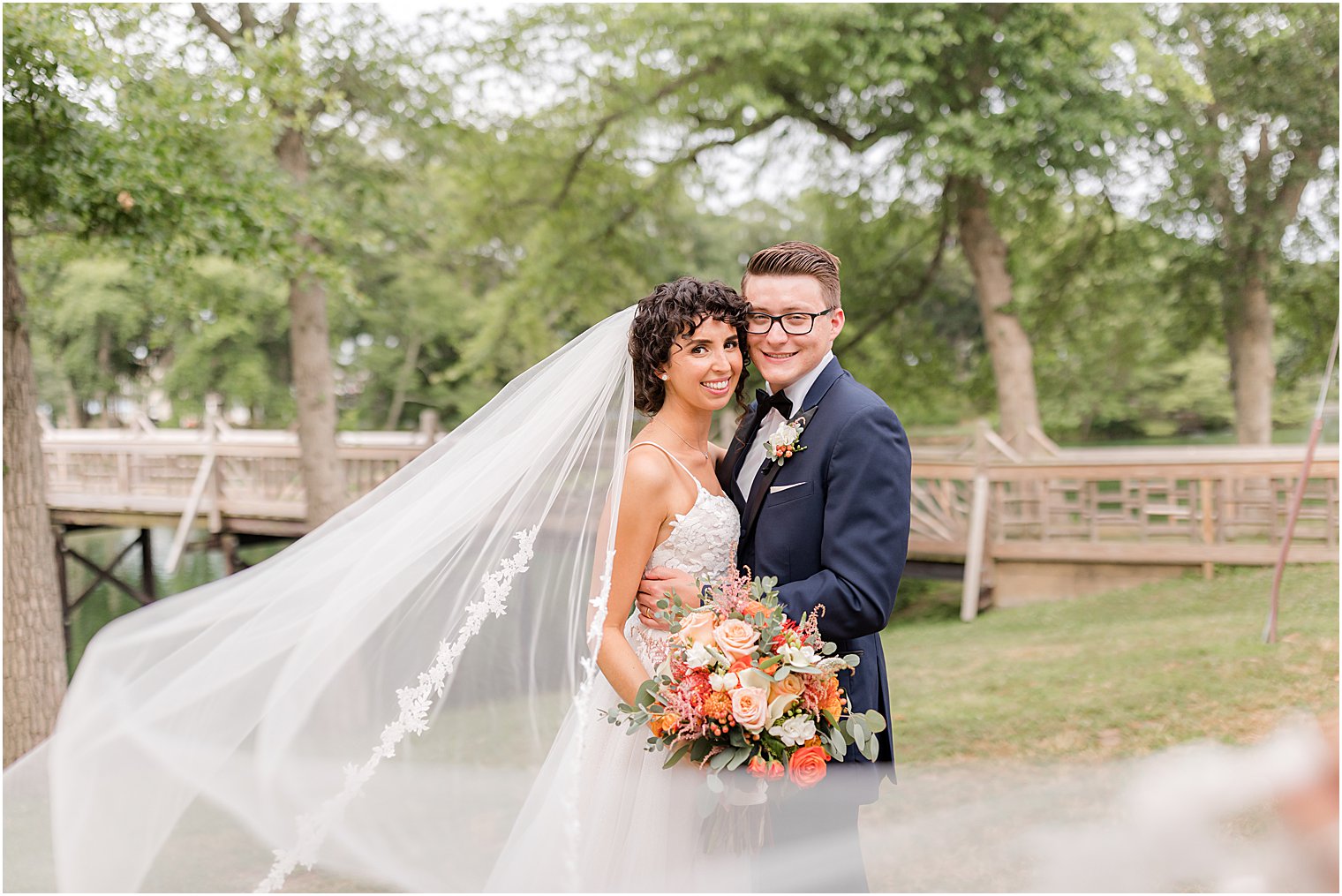 bride and groom hug by wooden bridge in Spring Lake Park with bride's veil around them