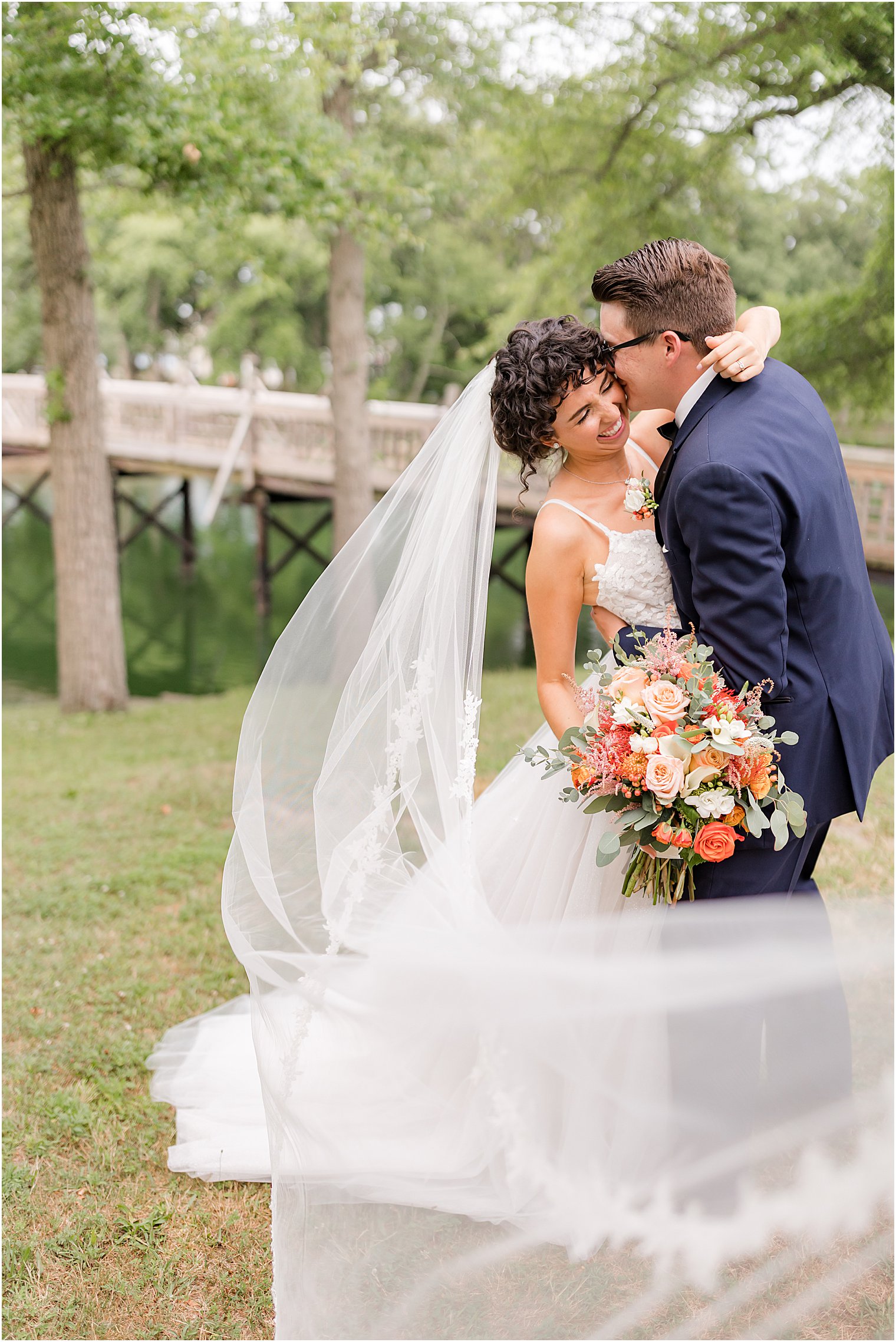 groom kisses bride's forehead with veil wrapped around them in Spring Lake Park
