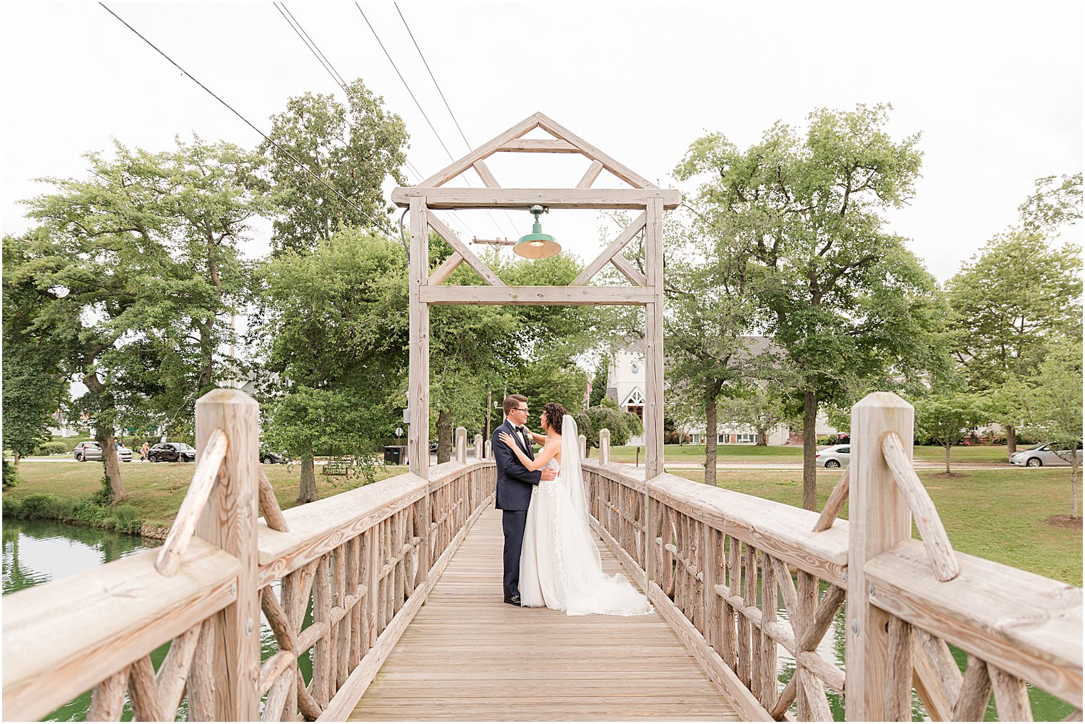 bride and groom stand on wooden bridge in Spring Lake Park