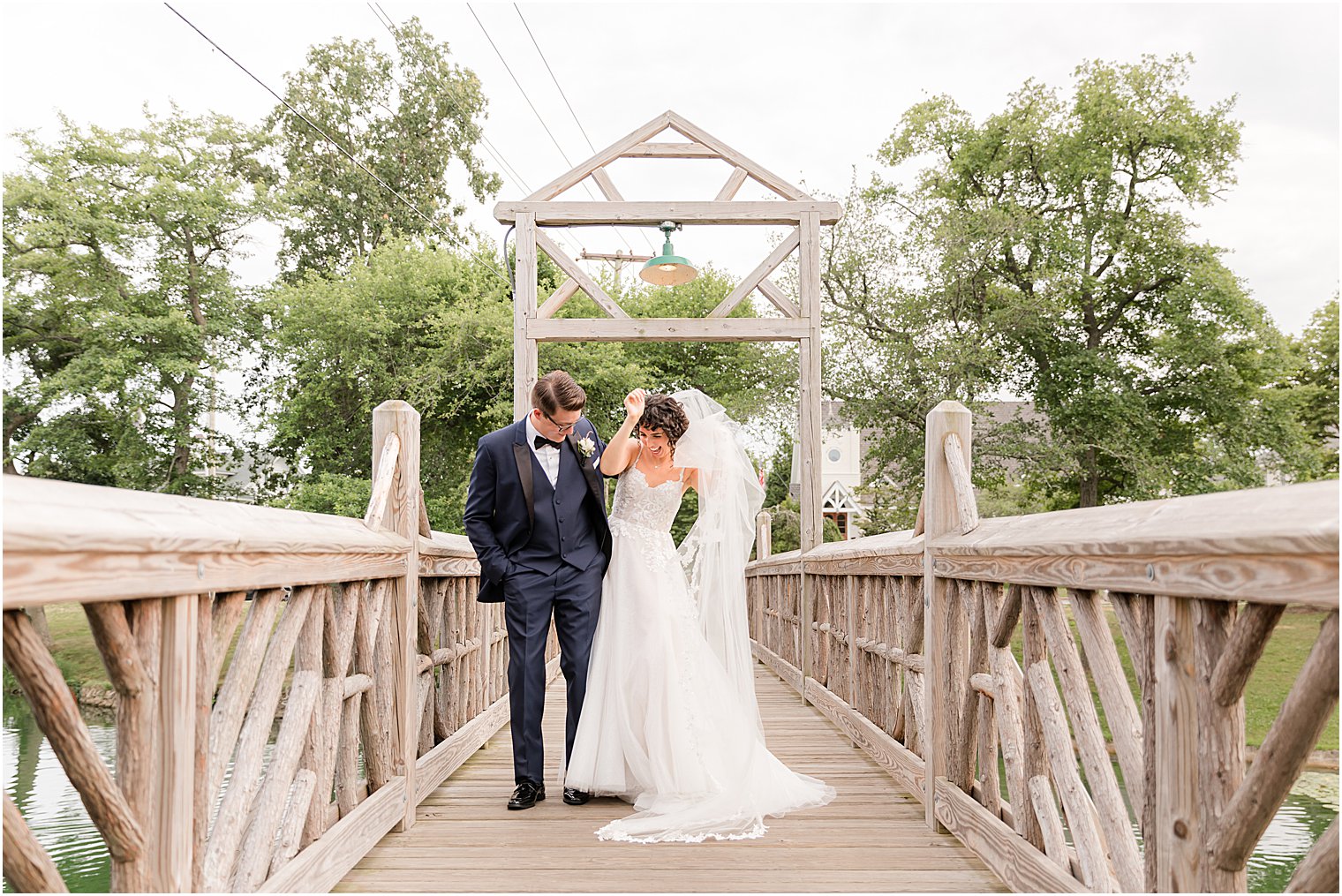newlyweds bump hips standing on bridge in Spring Lake Park