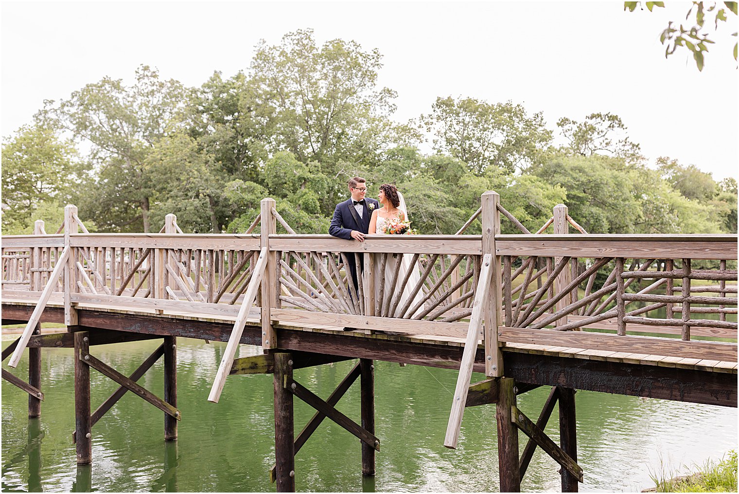 bride and groom stand together on bridge in Spring Lake Park