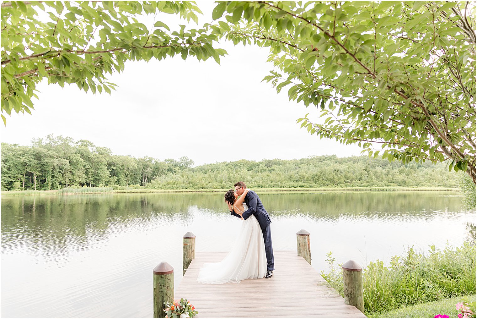 bride and groom kiss on dock during portraits at The Mill Lakeside Manor