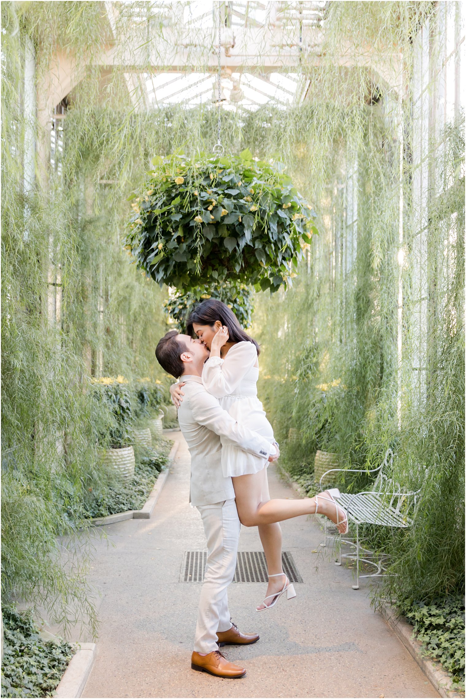 groom lifts bride up kissing her in gardens 