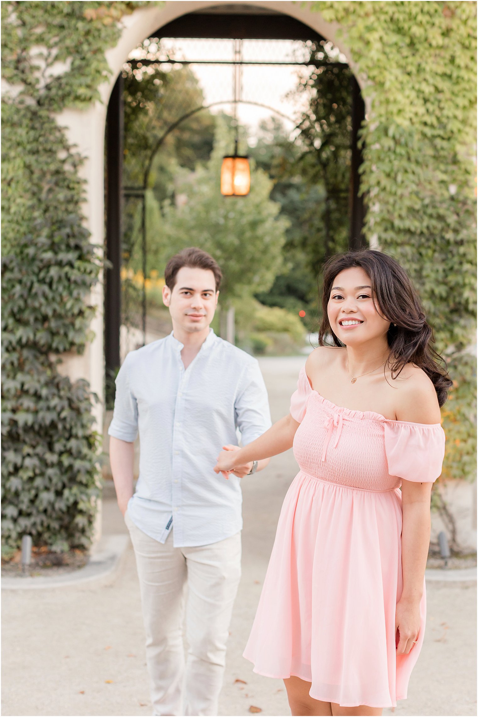 woman in pink dress leads fiancee through Longwood Gardens