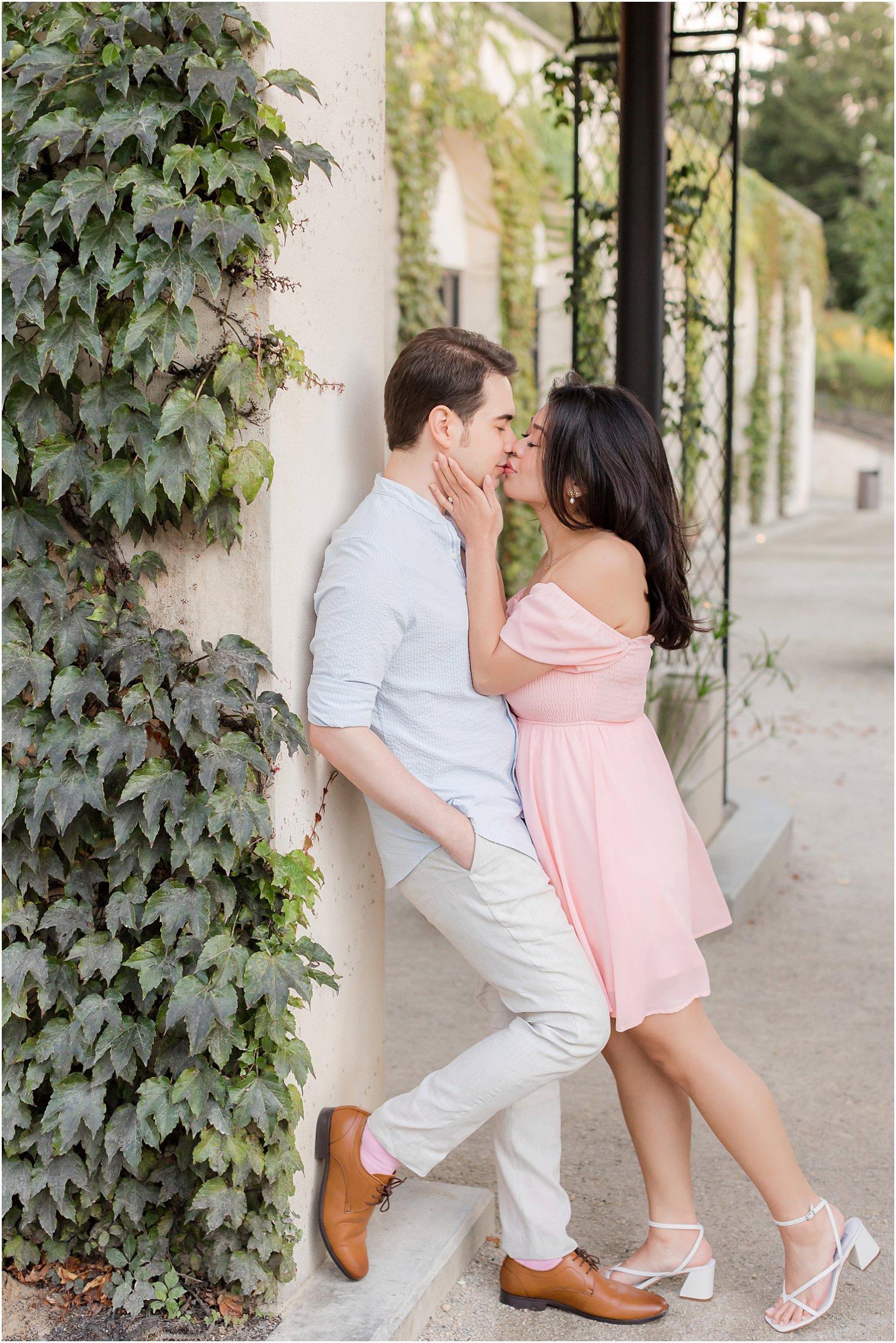 man and woman kiss leaning against tan wall at Longwood Gardens