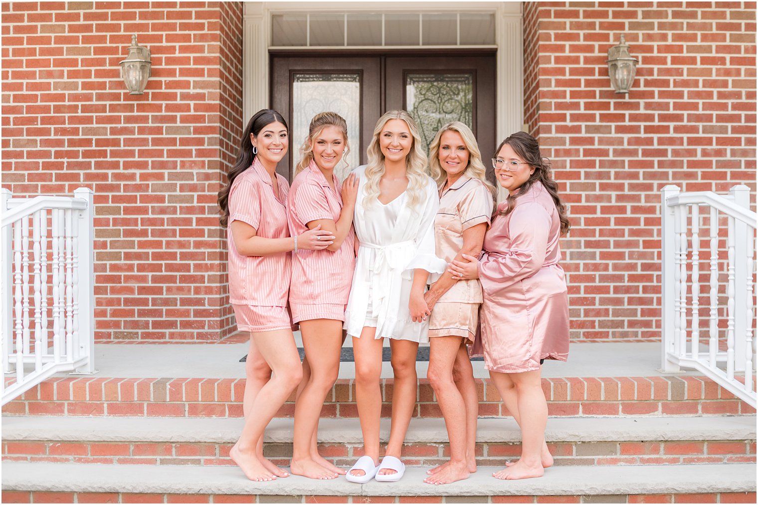 bride stands with bridesmaids in pink robes before wedding day