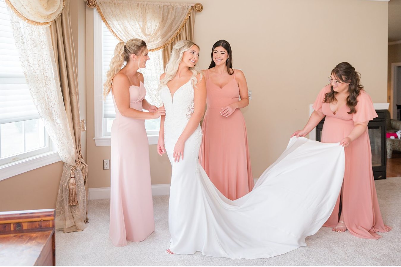 bride looks at bridesmaids helping her into gown