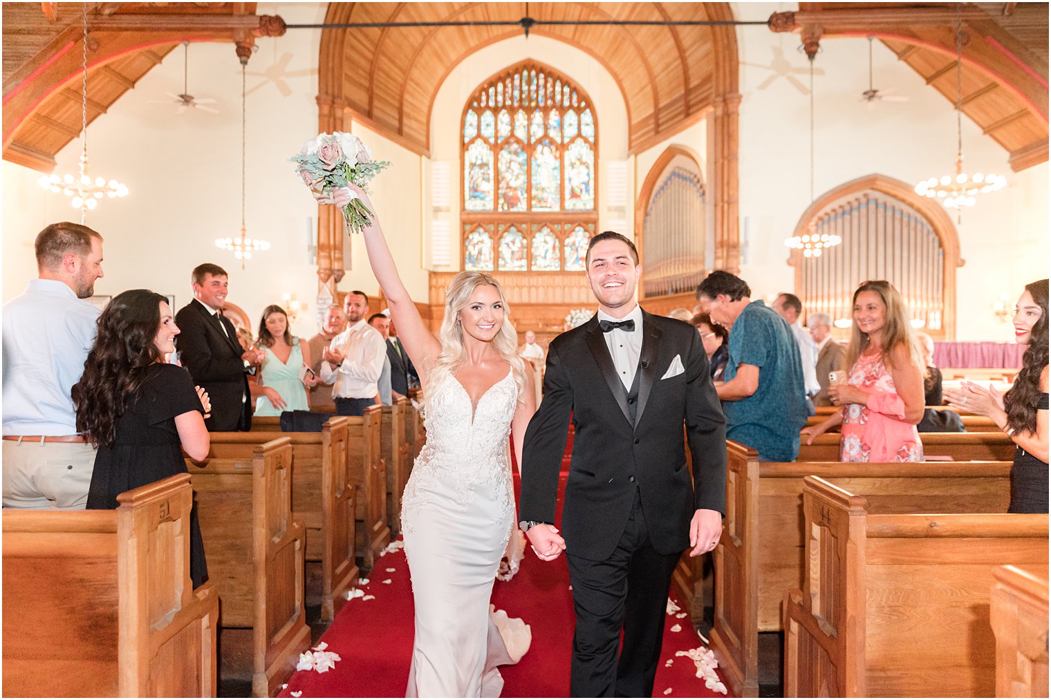 bride cheers lifting bouquet in the air leaving traditional church wedding in New Jersey