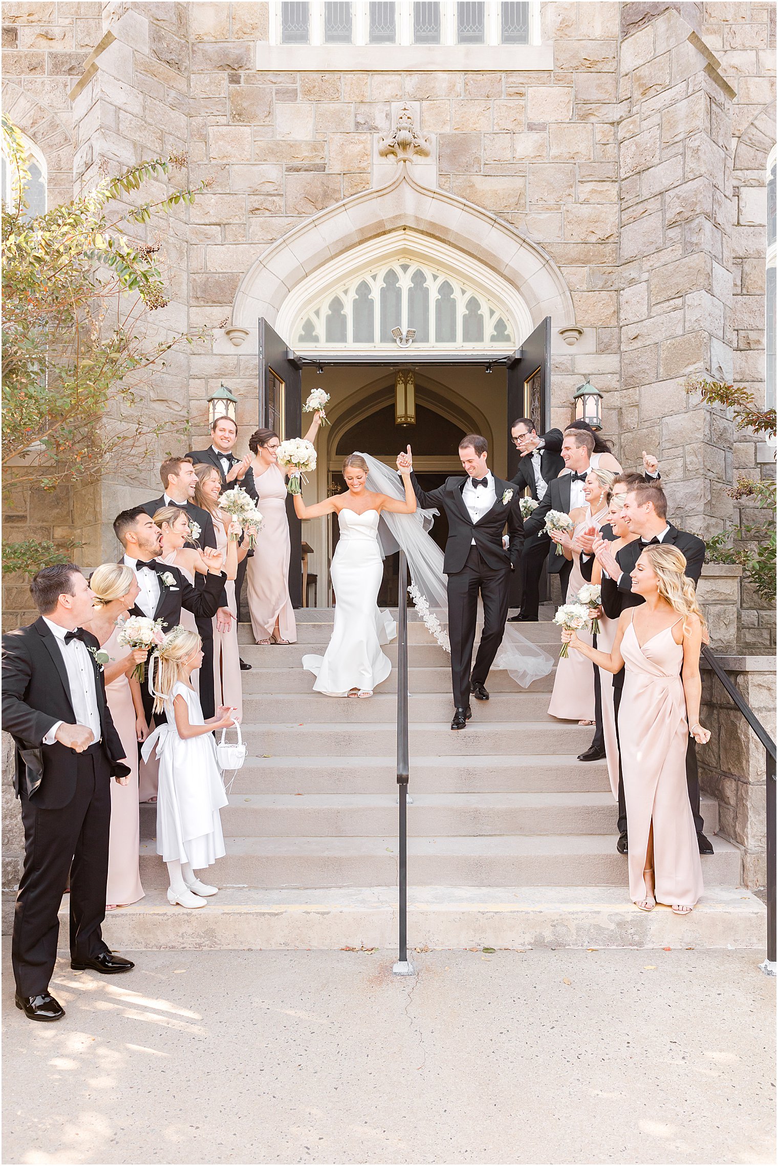 bride and groom leave traditional church wedding at St. Mary's Catholic Church with wedding party on steps cheering for them