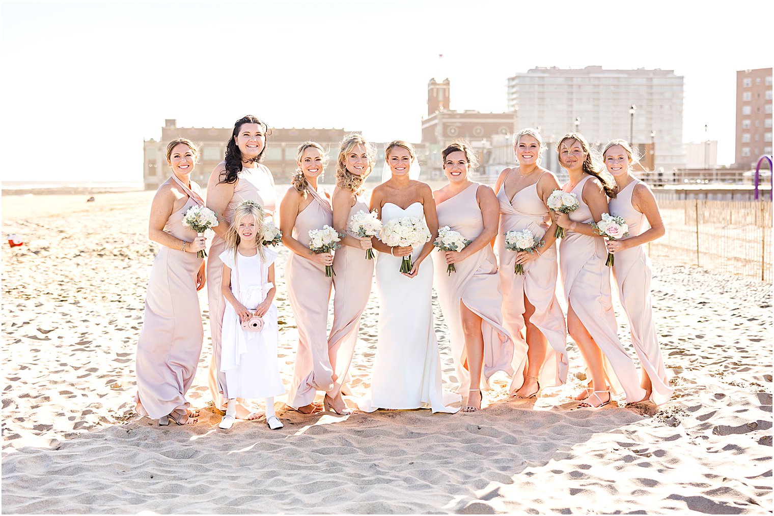 bride poses on beach with bridesmaids in pink gowns