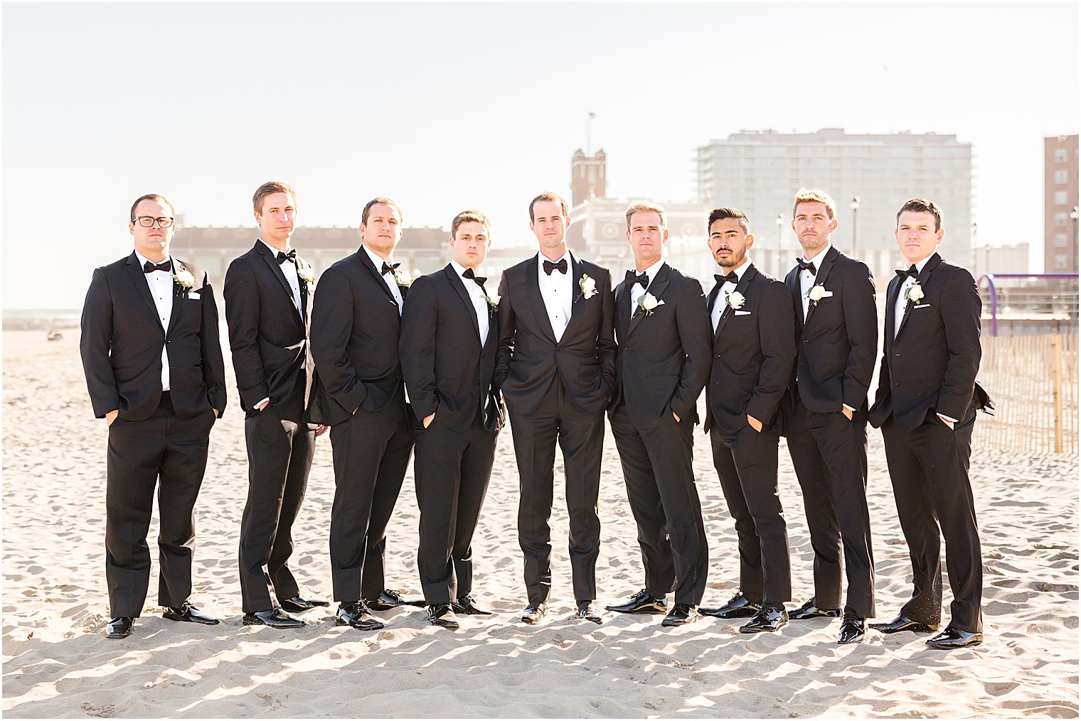 groom stands with groomsmen in black suits on beach at Asbury Park